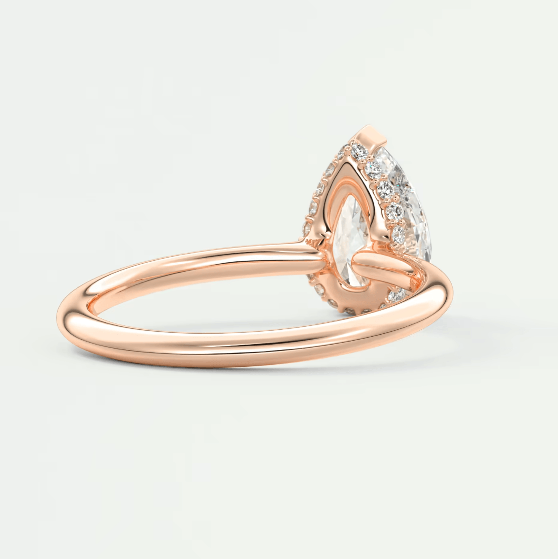 Rose gold pear-shaped diamond engagement ring with intricate floral detailing and halo of smaller diamonds.