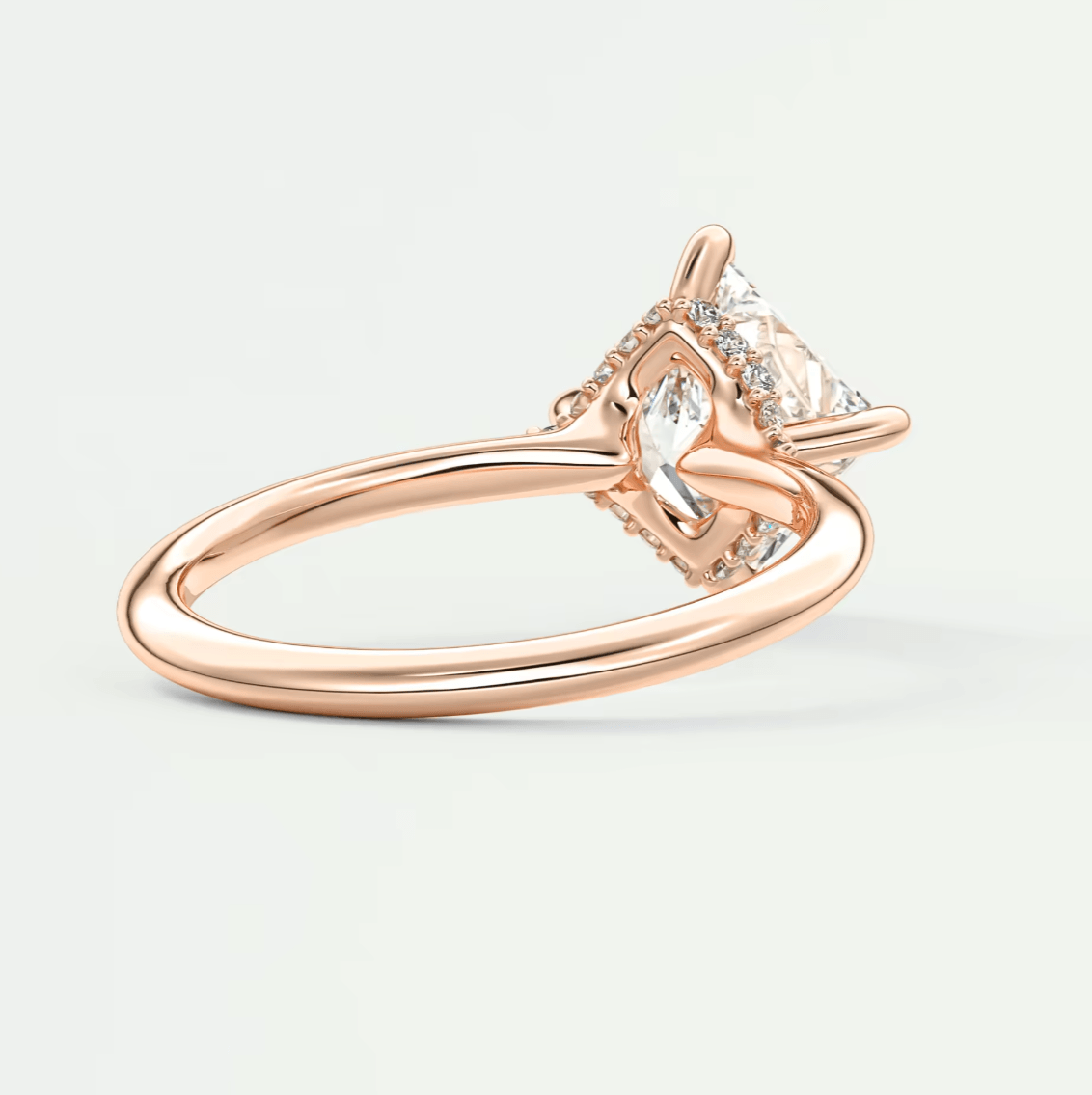 Rose gold engagement ring with a princess cut diamond and halo of smaller diamonds, featuring an elegant design.