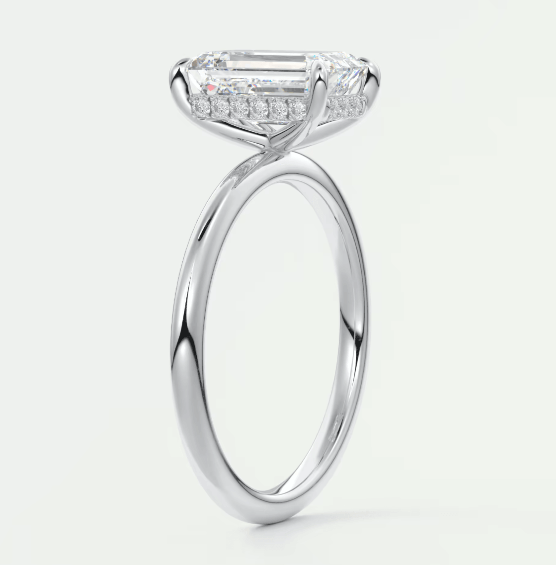 18-karat white gold engagement ring with an emerald-cut diamond and pavé side stones.