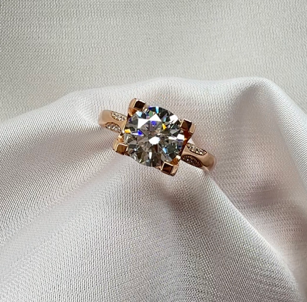 Rose gold ring with a large diamond on a white fabric background