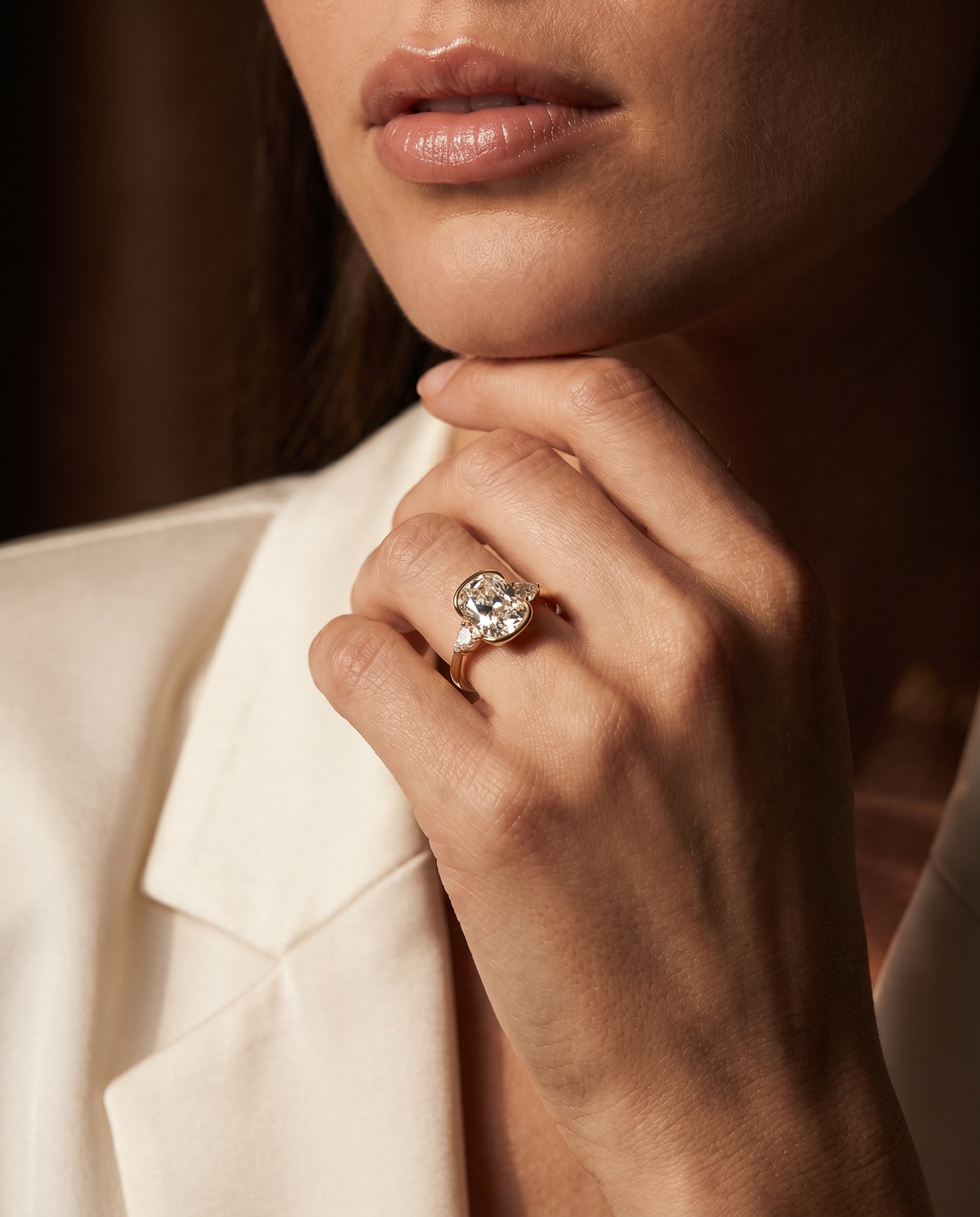 A close-up lifestyle shot of a model wearing a rose gold ring with a round-cut clear gemstone on her finger, paired with a cream-colored blazer.