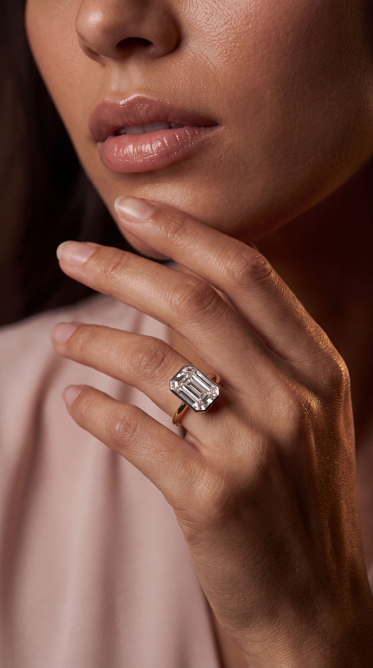 A close-up lifestyle shot of a model wearing a gold ring with a large rectangular emerald-cut clear gemstone on her finger.