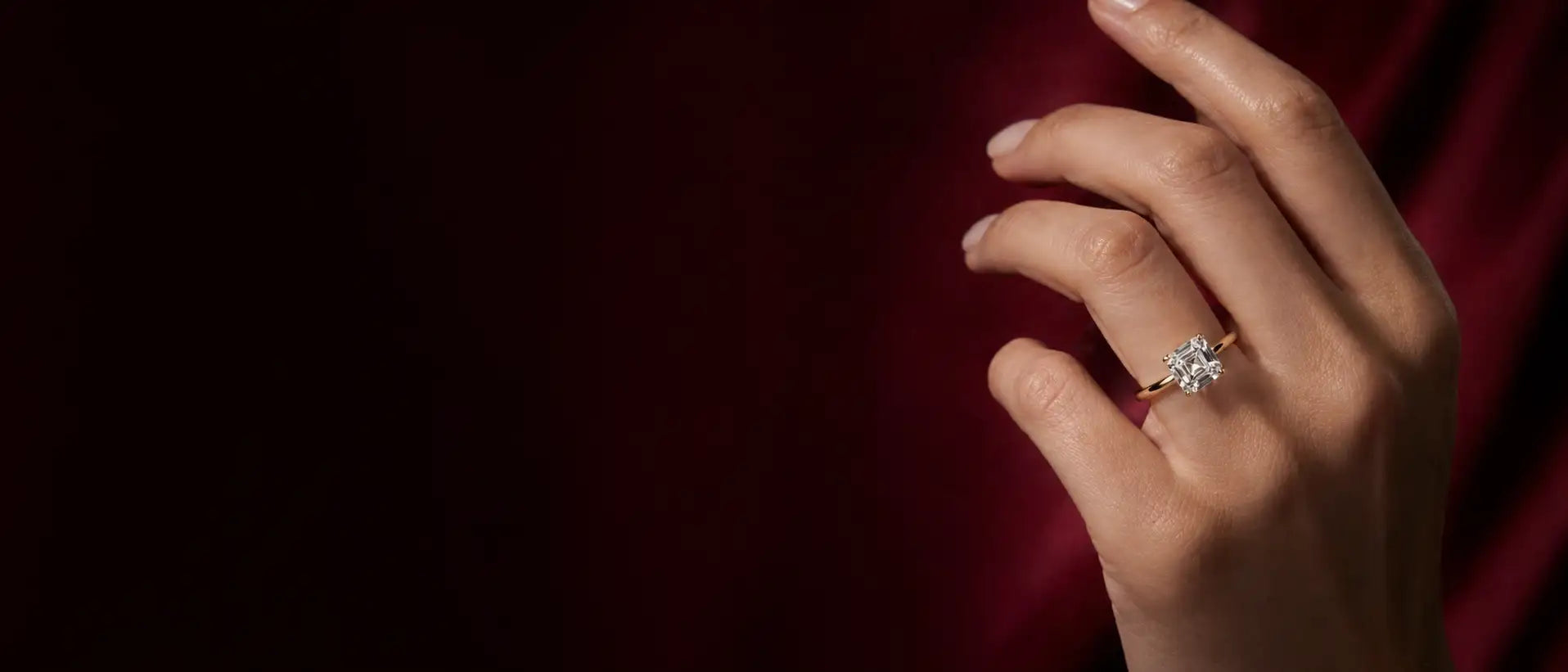 Hand wearing a diamond ring against a dark red background