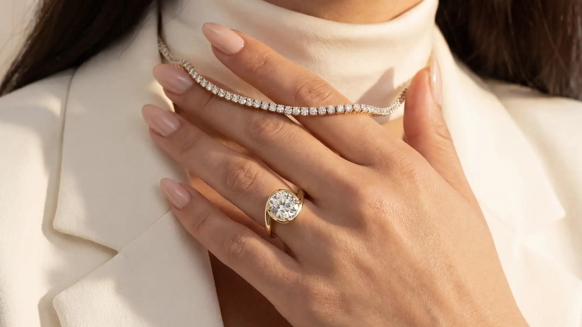 Close-up of a hand wearing a diamond ring and holding a diamond necklace.
