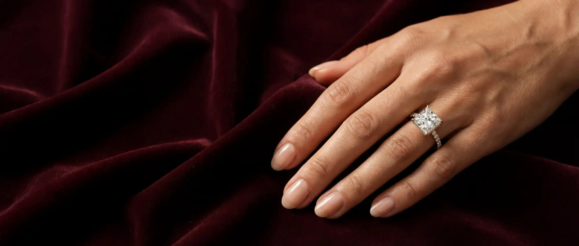 Hand wearing a diamond ring on a dark red fabric background