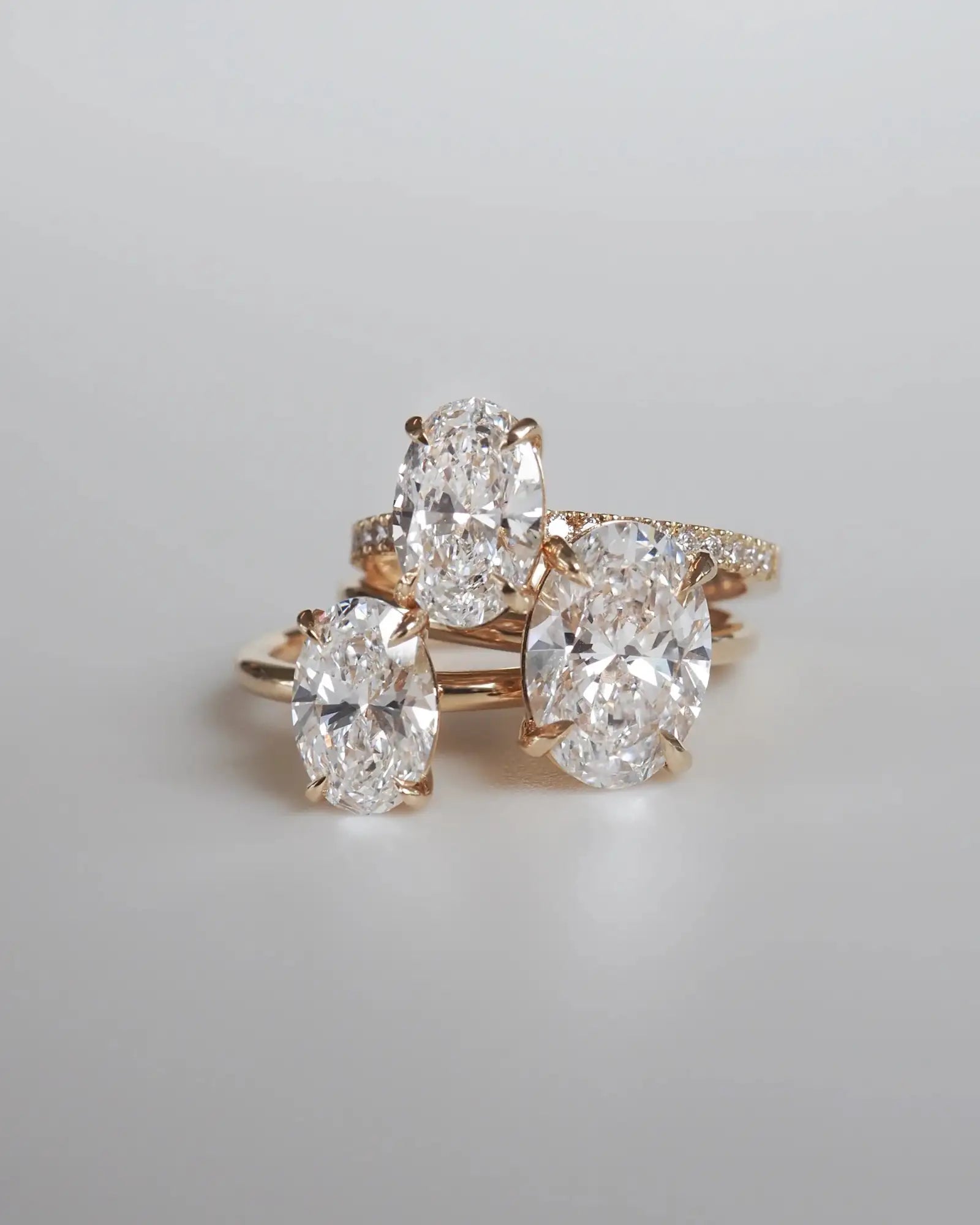 Three elegant rose gold engagement rings, each featuring a prominent oval-cut diamond center with smaller diamonds encircling the band.