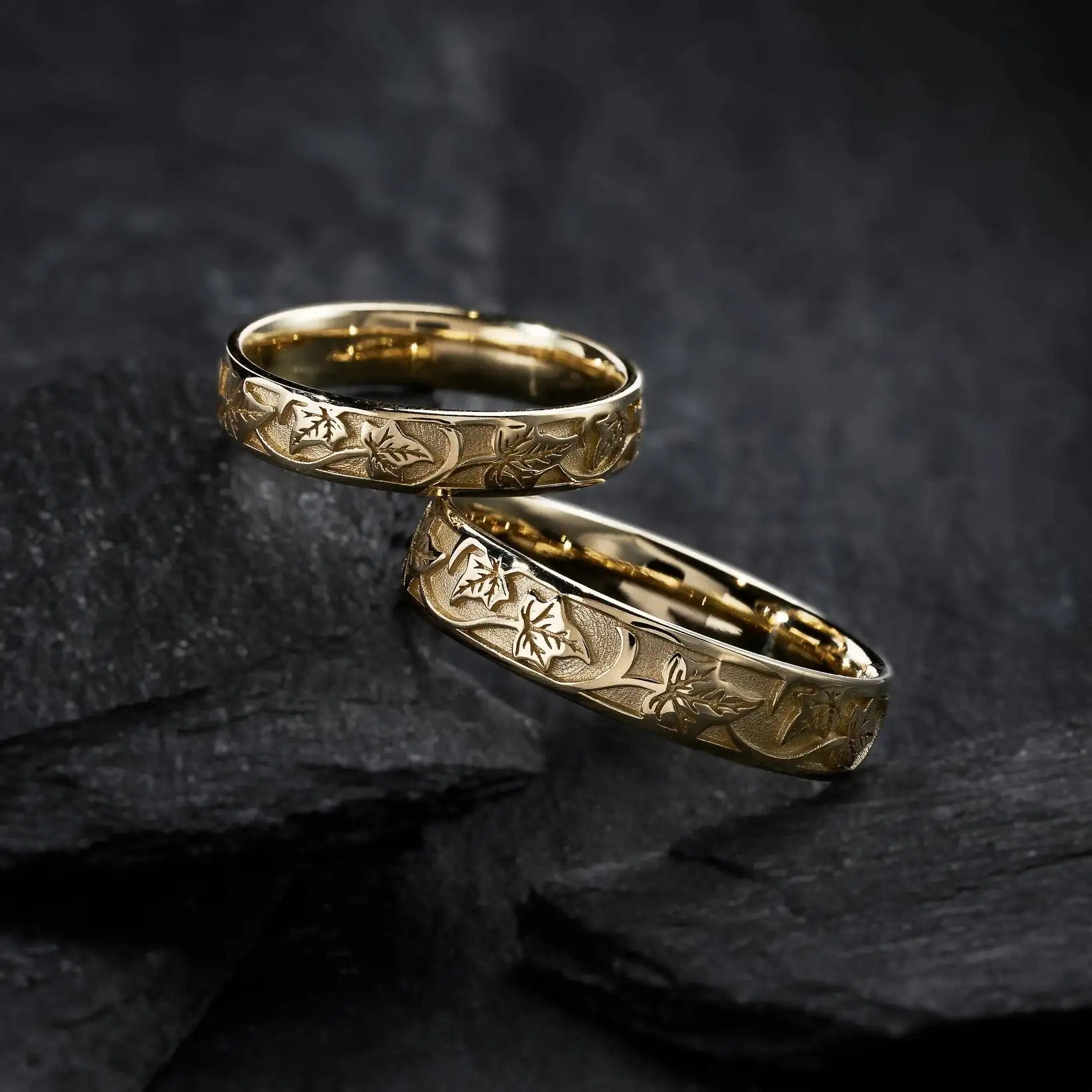 Two gold rings with intricate designs on a dark textured surface