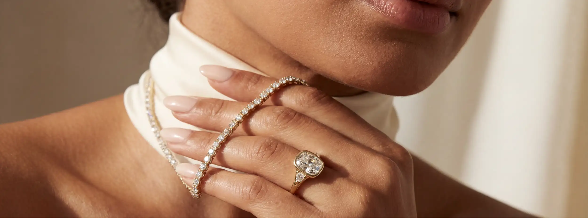 Close-up of a woman's hand wearing a diamond ring and bracelet against a neutral background