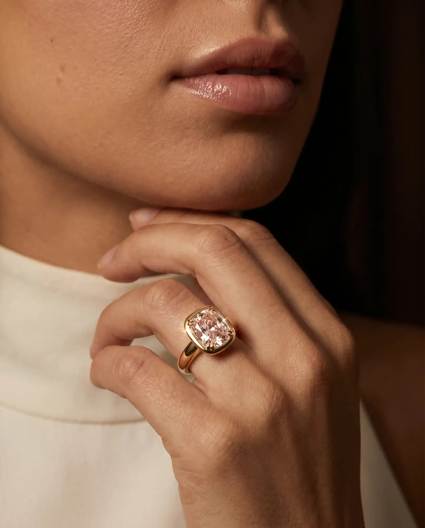 A close-up lifestyle shot of a model wearing a rose gold ring with a cushion-cut pink lab diamond.