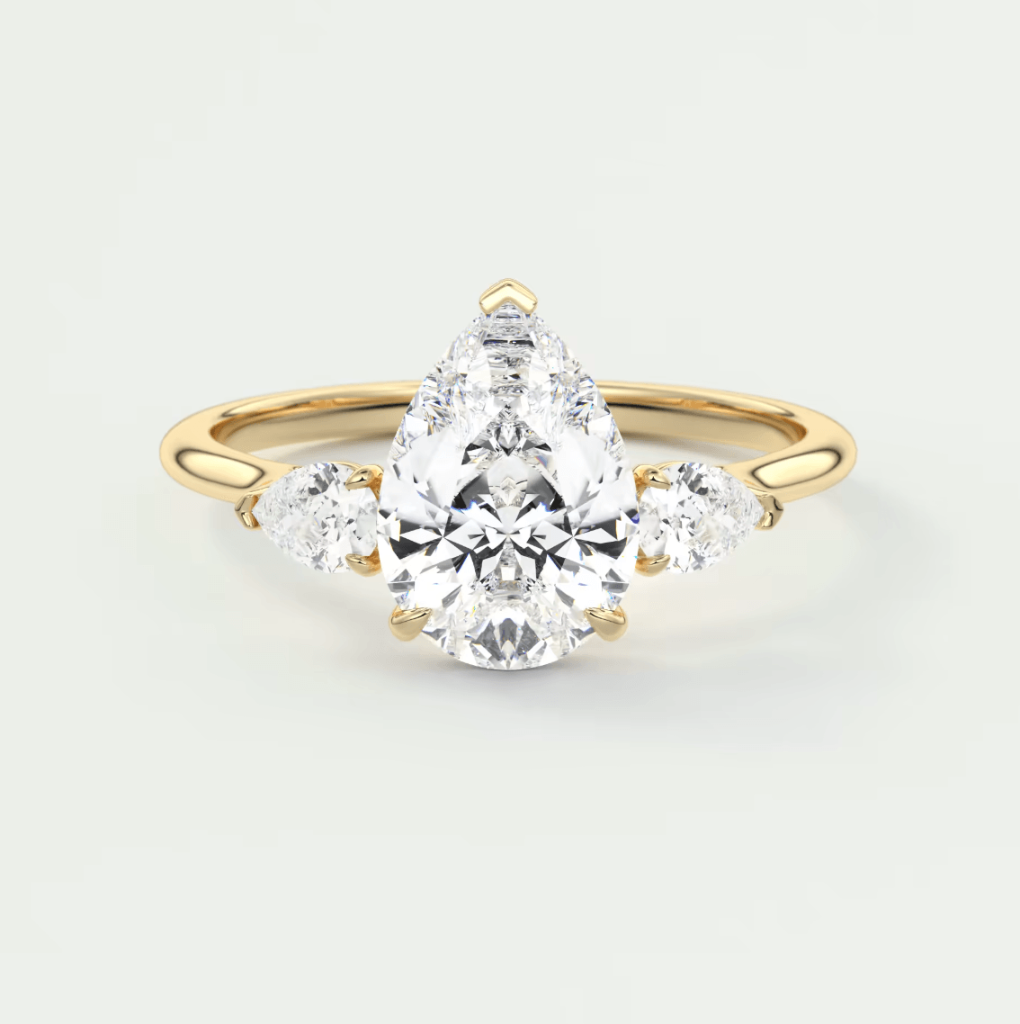 Pear-shaped diamond engagement ring with three smaller diamonds, set in yellow gold.