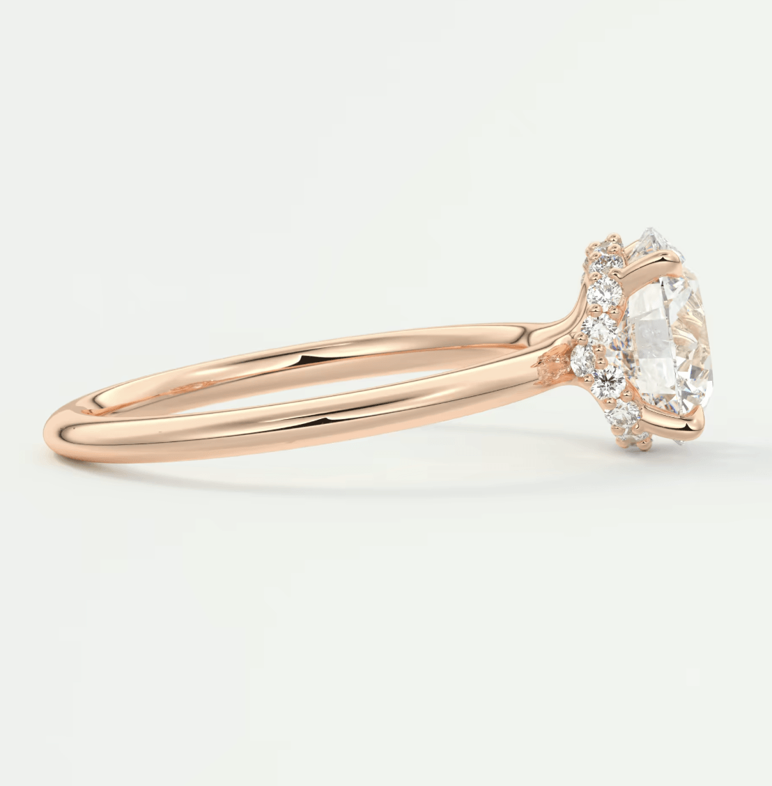 18-karat rose gold engagement ring with a central oval diamond and halo of smaller diamonds.