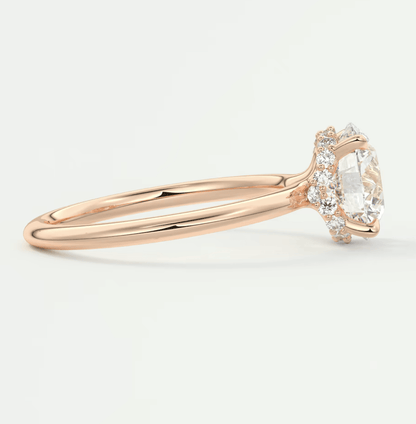 18-karat rose gold engagement ring with a central oval diamond and halo of smaller diamonds.