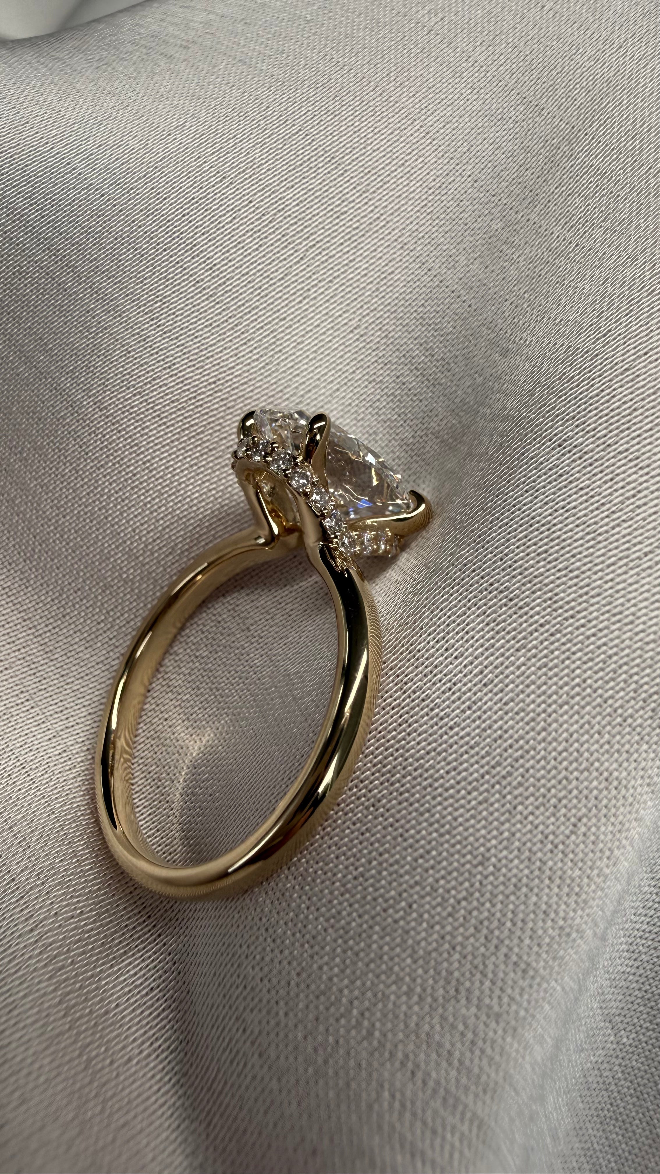 A gold ring with a large pear-cut clear center stone and small clear accent stones, photographed on a textured light fabric background.