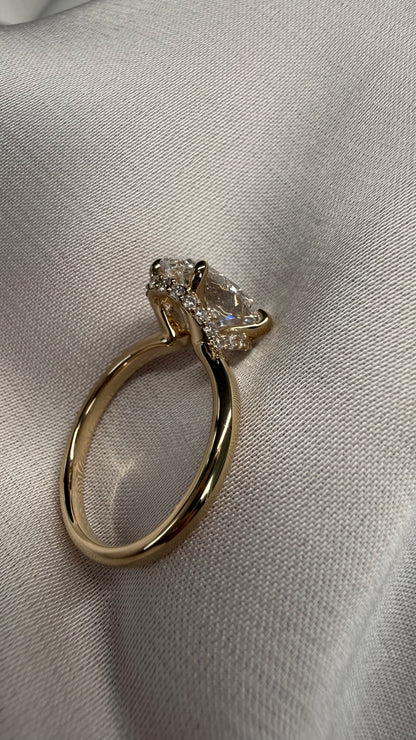 A gold ring with a large pear-cut clear center stone and small clear accent stones, photographed on a textured light fabric background.