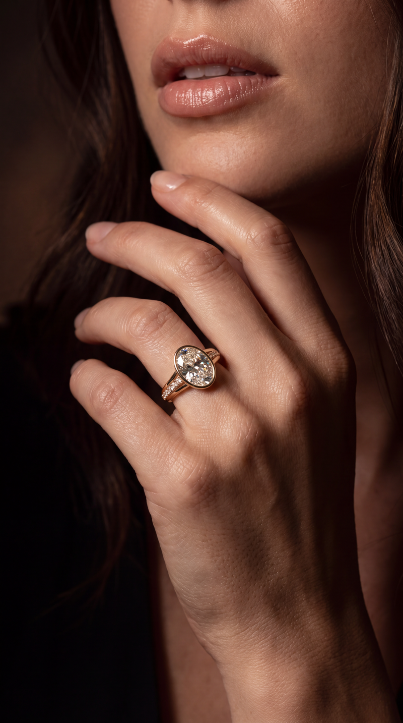 A close-up lifestyle shot of a woman's hand wearing a gold ring with a heart-shaped clear gemstone, set against a dark, moody background.