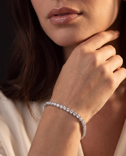 A close-up lifestyle shot of a woman wearing a sparkling diamond tennis bracelet on her wrist, with her hand resting near her chin.