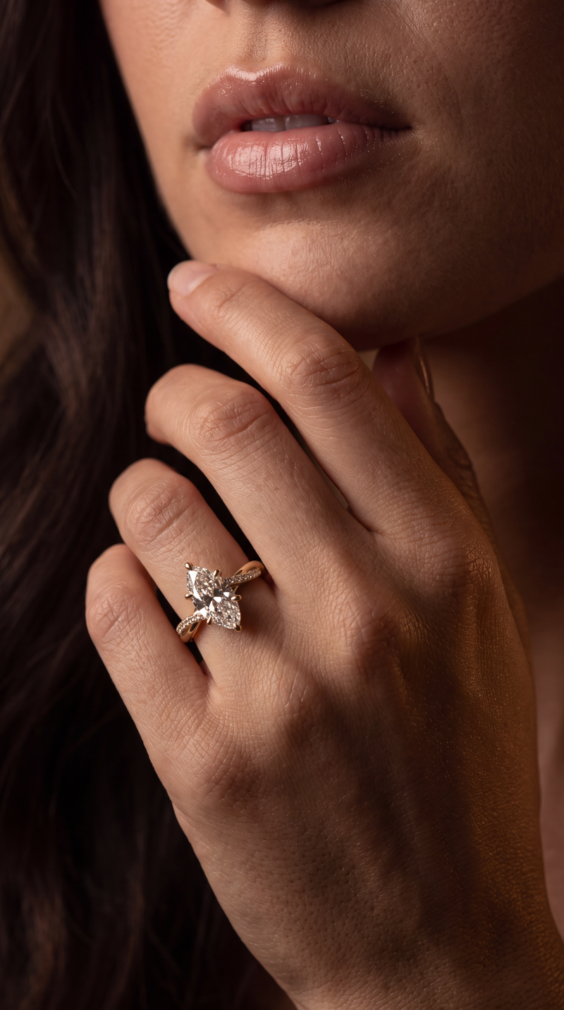 A close-up lifestyle shot of a woman's hand resting near her chin, wearing a delicate gold ring with a small, clear, diamond-like floral cluster setting.