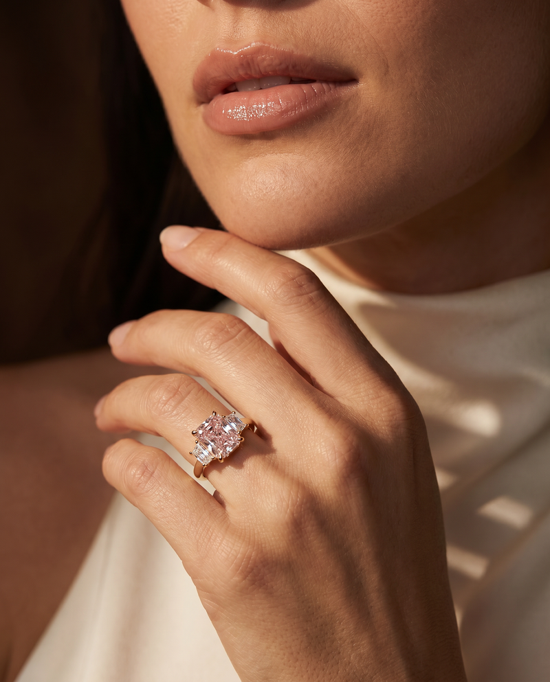 A close-up lifestyle shot of a model wearing a rose gold ring with a large cluster of clear gemstones on her finger.