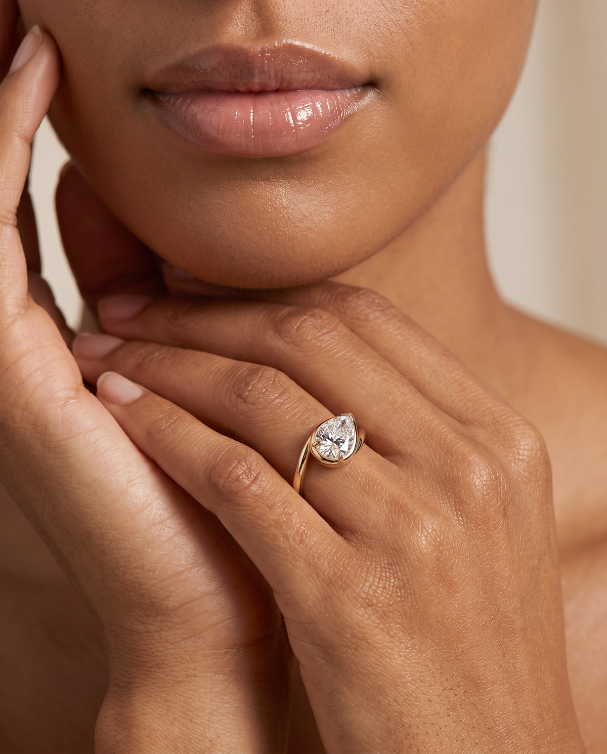 A close-up lifestyle shot of a model wearing a yellow gold ring with a pear-cut clear gemstone, resting her hands on her lap.