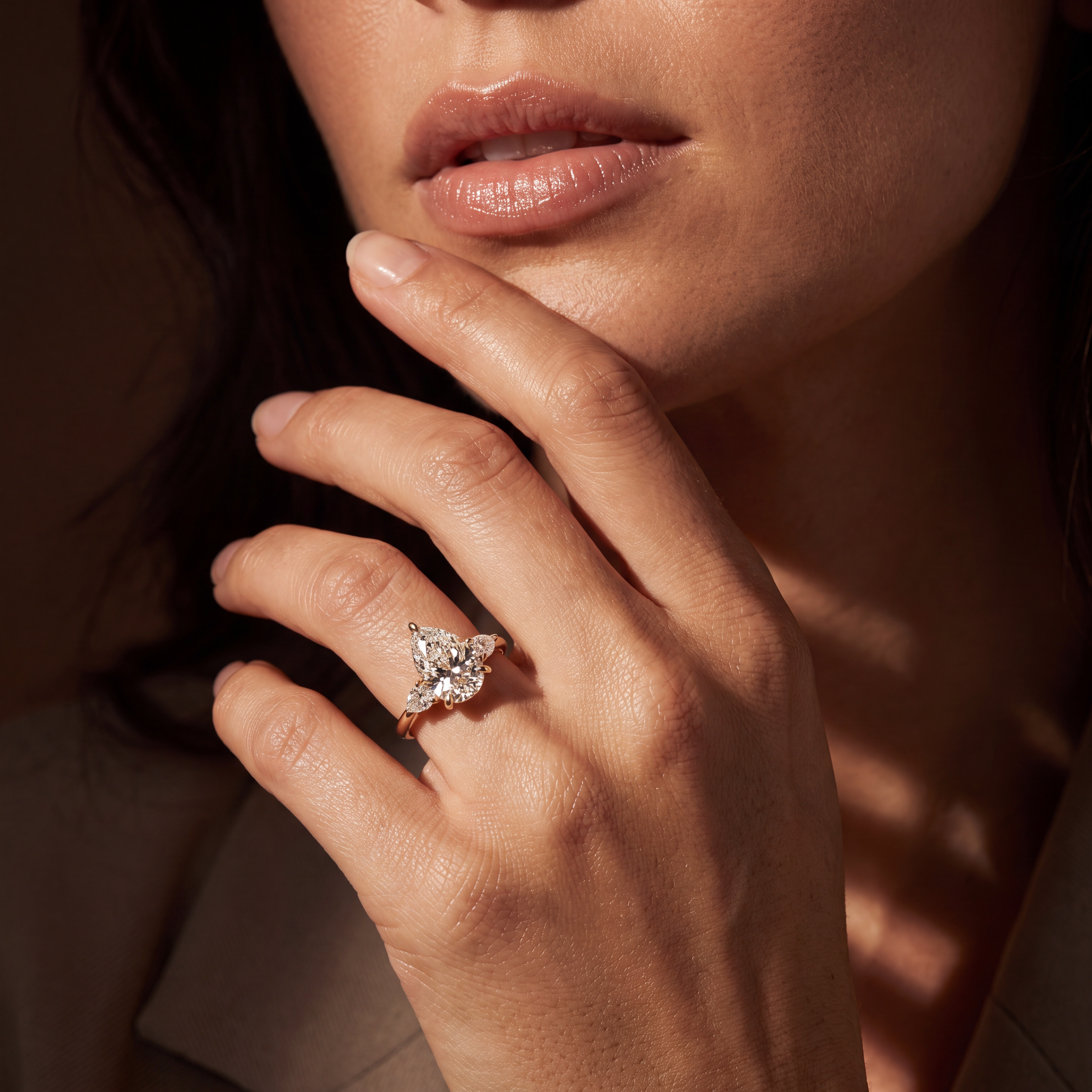 A close-up lifestyle shot of a woman's hand wearing a rose gold ring with a diamond butterfly cluster setting, set against a dark background with warm sunlight shadows.