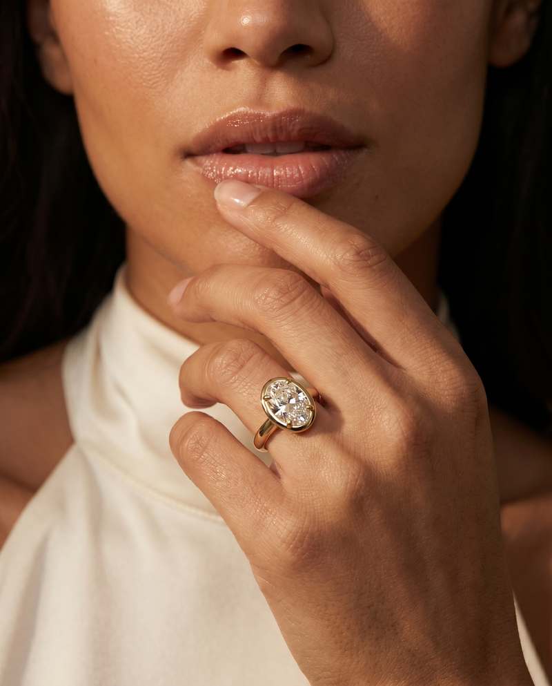 A close-up lifestyle shot of a model wearing a rose gold ring with a cluster of clear gemstones on her finger.