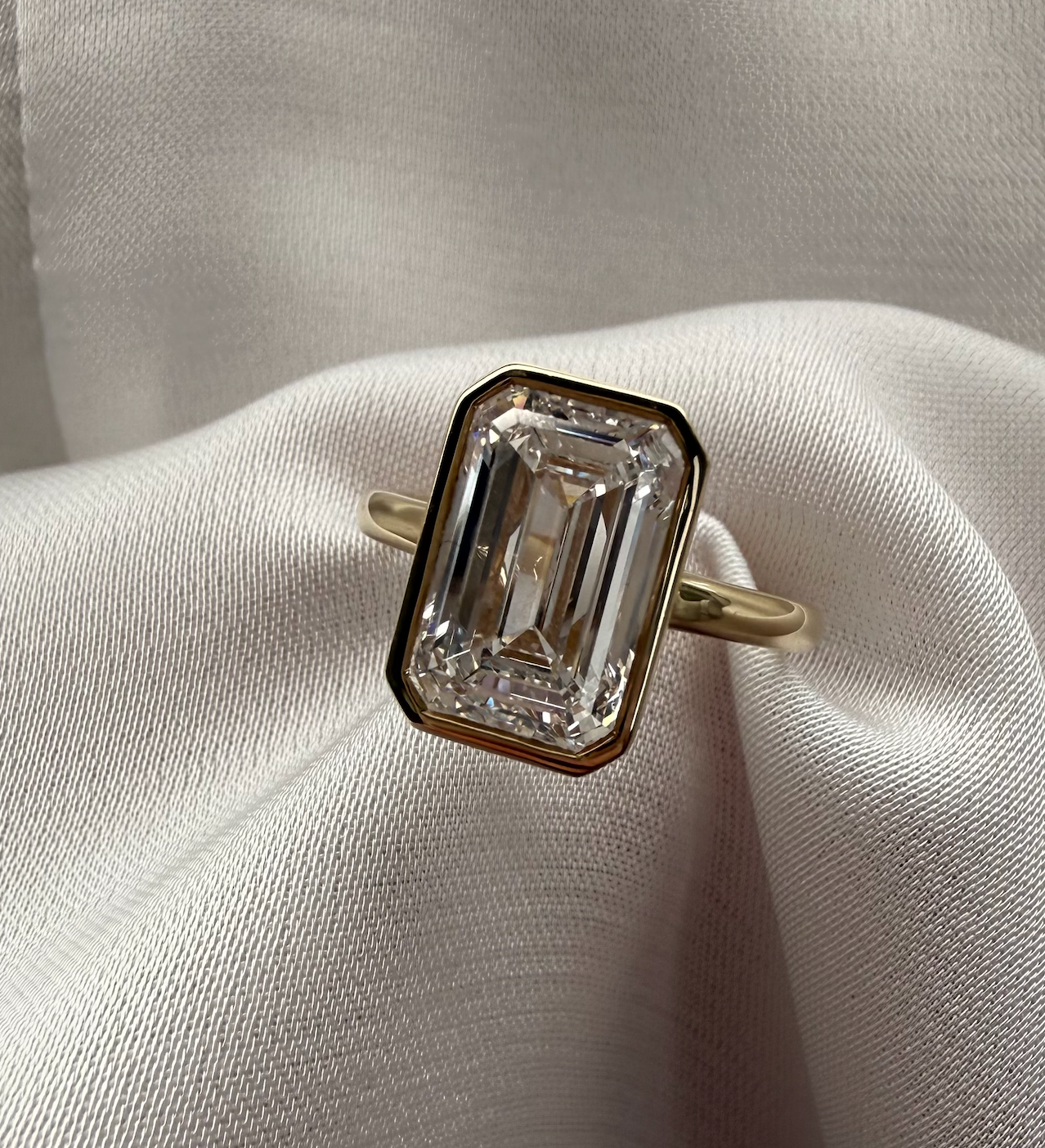 Diamond ring with emerald-cut stone on a white fabric background