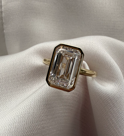 Diamond ring with emerald-cut stone on a white fabric background