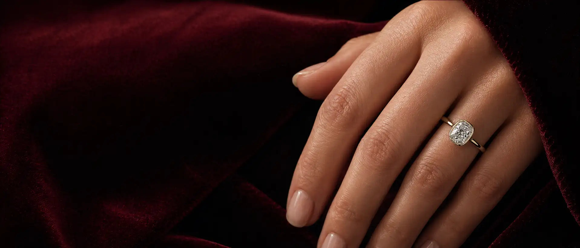 Close-up of a hand wearing an engagement ring on a dark fabric background