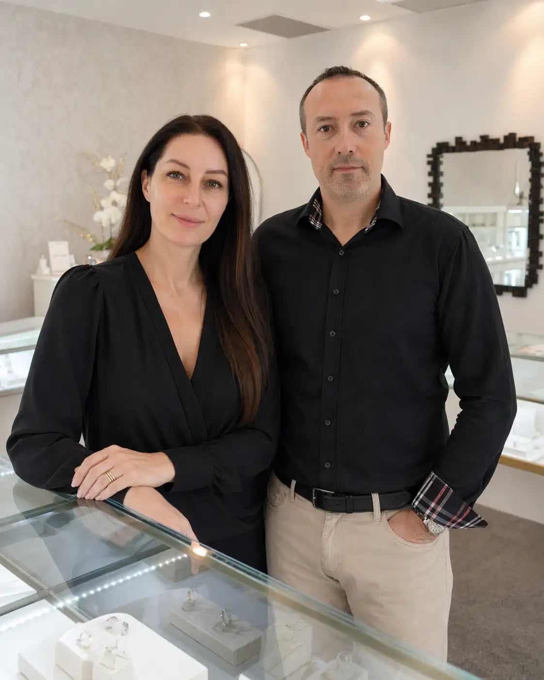 Two people standing in a room with a glass display case containing jewelry.