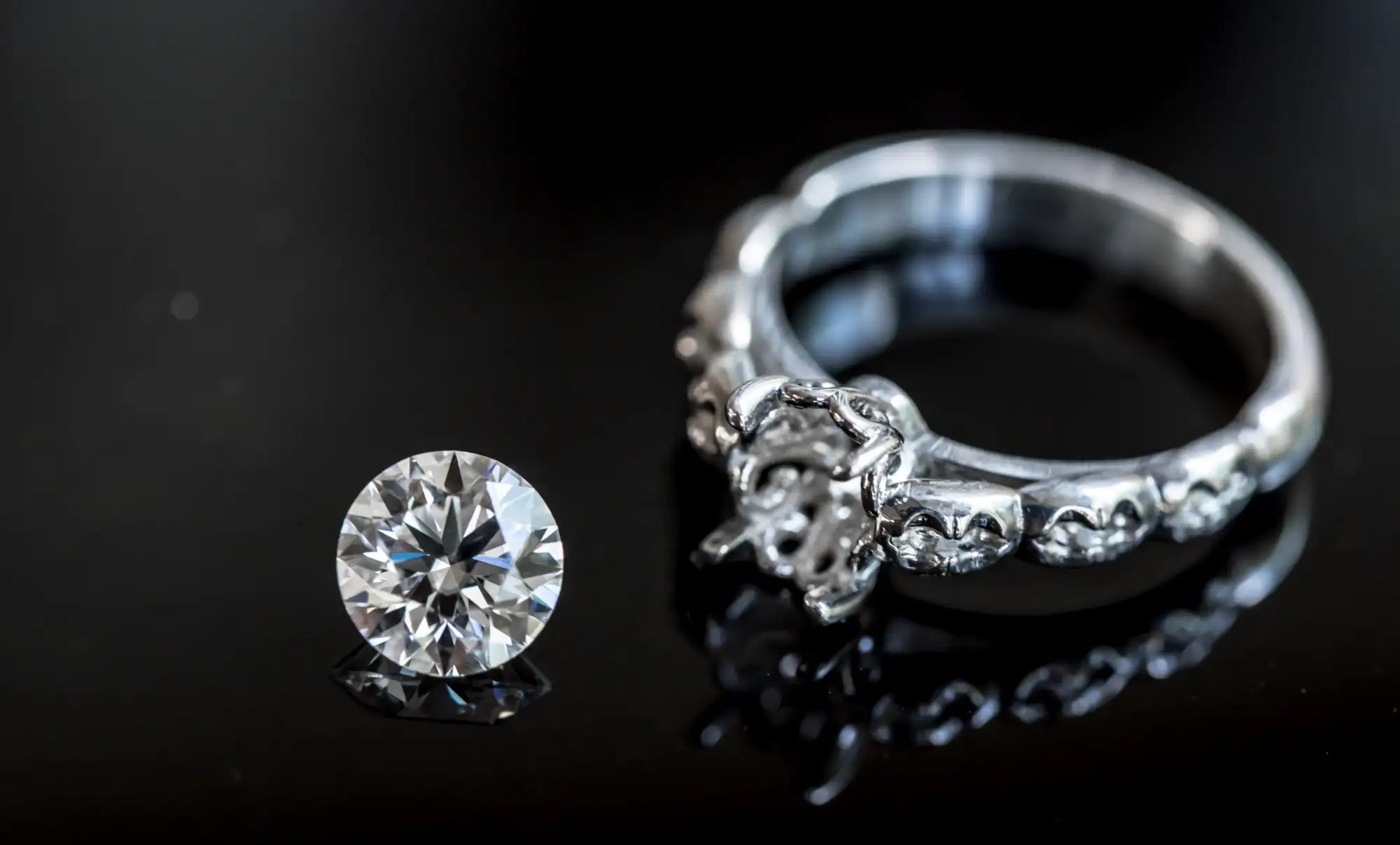 A sparkling round-cut diamond rests beside an ornate silver ring with intricate detailing and embedded stones.