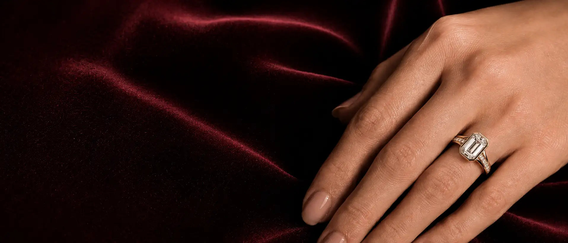 Hand wearing a diamond ring on a dark red fabric background